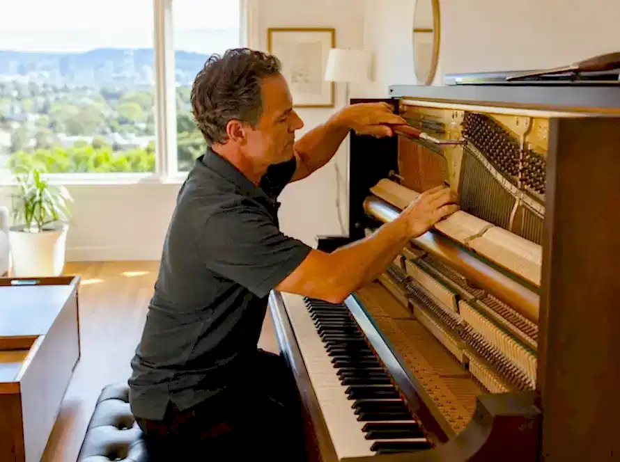 Piano technician near me tuning an upright piano inside a bright modern Bay Area home using professional piano tuning tools.